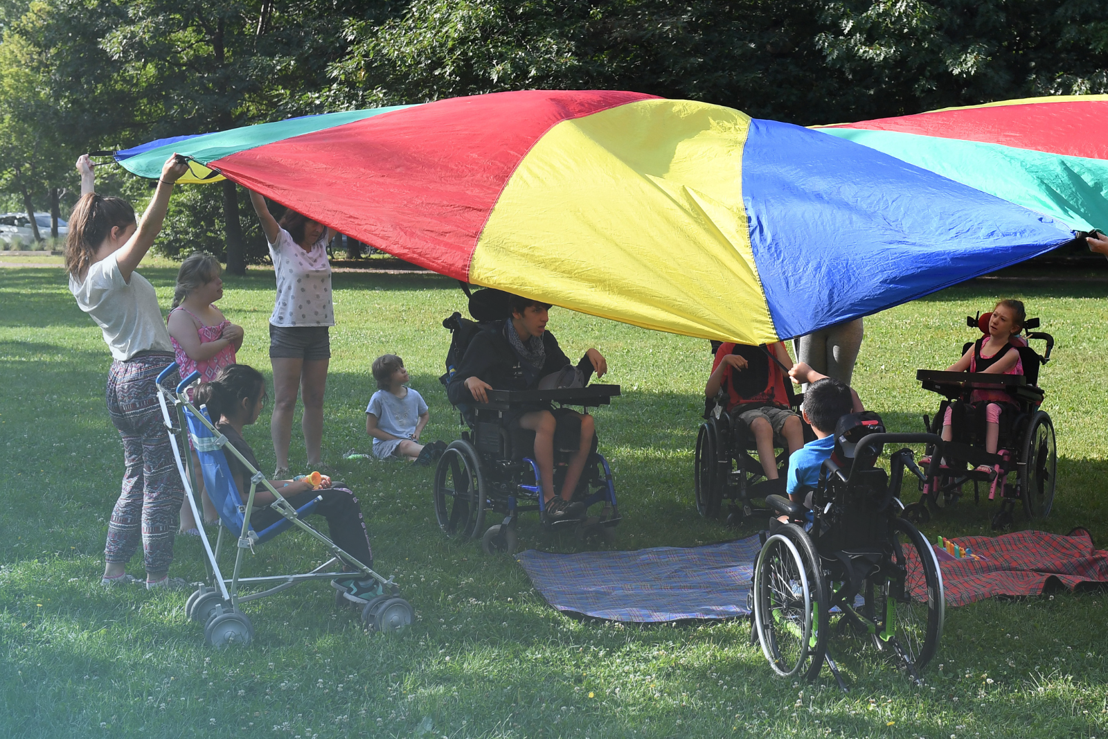 Des enfants ayant une limitation fonctionnelle s'amusent dans un parc avec un grand parachute multicolore.